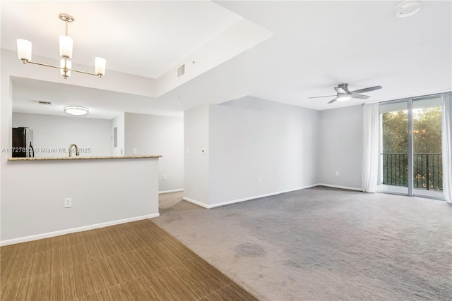 unfurnished living room featuring ceiling fan with notable chandelier, expansive windows, and carpet