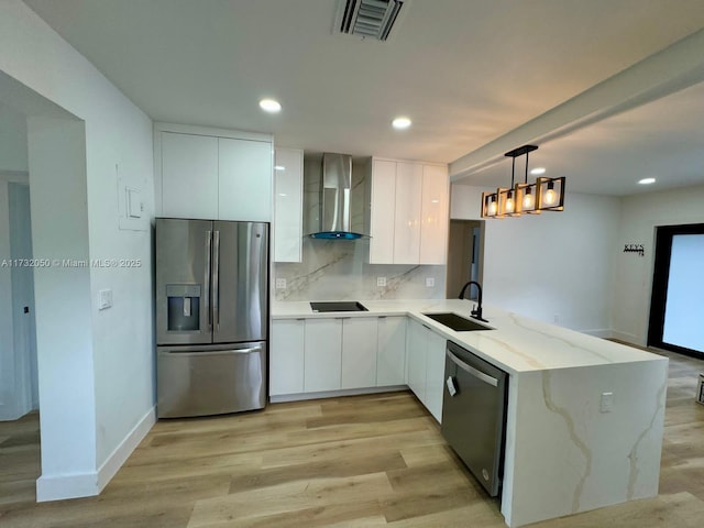 kitchen with pendant lighting, appliances with stainless steel finishes, white cabinetry, kitchen peninsula, and wall chimney exhaust hood