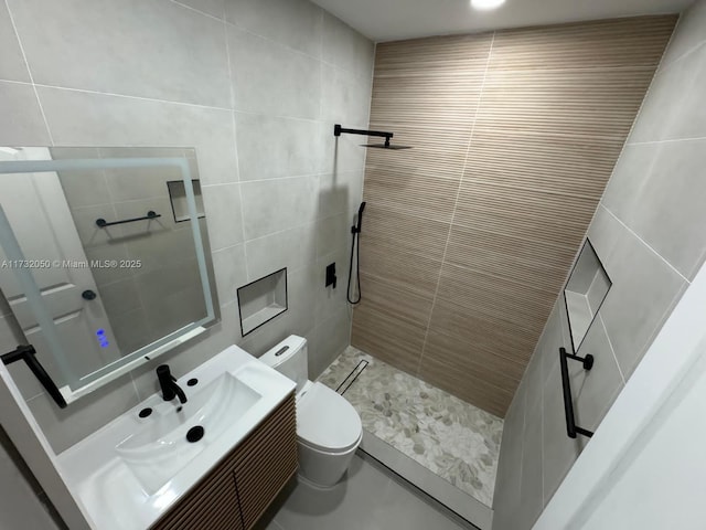 bathroom with vanity, tiled shower, tile walls, and toilet