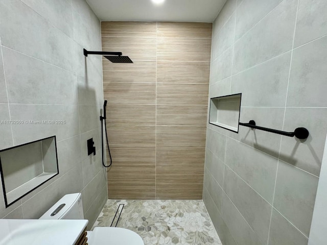 bathroom with vanity, tiled shower, tile walls, and toilet