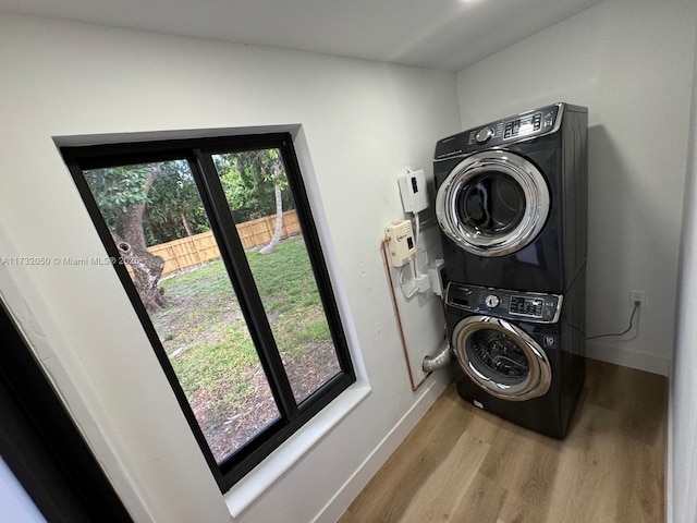 laundry room featuring light wood-type flooring, plenty of natural light, and stacked washing maching and dryer