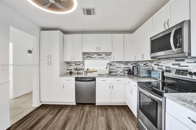 kitchen featuring sink, appliances with stainless steel finishes, white cabinetry, light stone counters, and dark hardwood / wood-style flooring