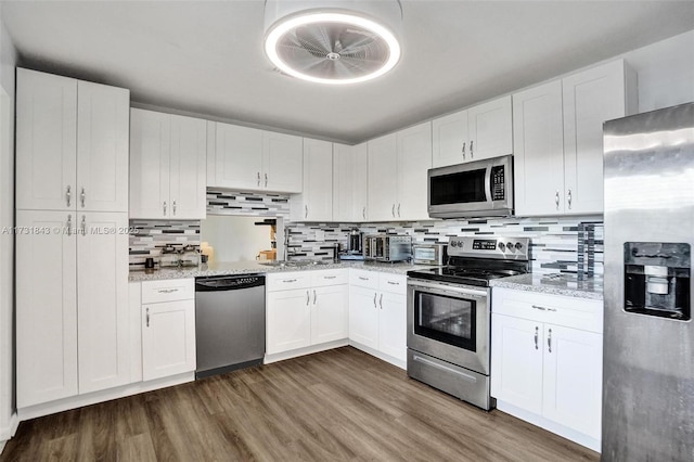 kitchen with appliances with stainless steel finishes, dark wood-type flooring, white cabinets, and light stone counters