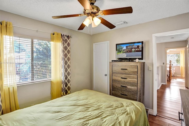 bedroom featuring multiple windows, hardwood / wood-style floors, a textured ceiling, and ceiling fan