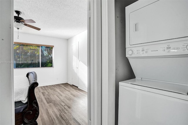 laundry area with ceiling fan, stacked washing maching and dryer, light hardwood / wood-style floors, and a textured ceiling