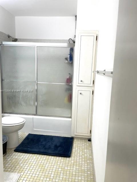 bathroom with toilet and bath / shower combo with glass door