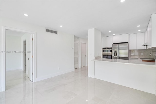 kitchen with sink, white cabinetry, kitchen peninsula, stainless steel appliances, and decorative backsplash