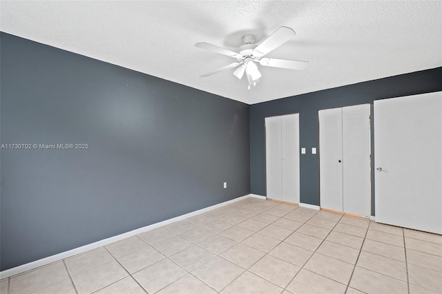 unfurnished bedroom with light tile patterned flooring, two closets, a textured ceiling, and ceiling fan