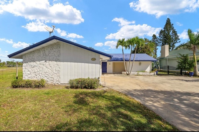 view of side of home featuring driveway, stone siding, metal roof, fence, and a yard