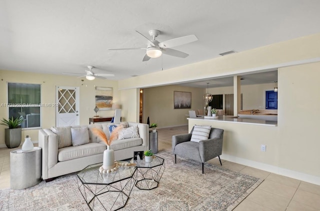 living room featuring light tile patterned floors, ceiling fan with notable chandelier, visible vents, and baseboards