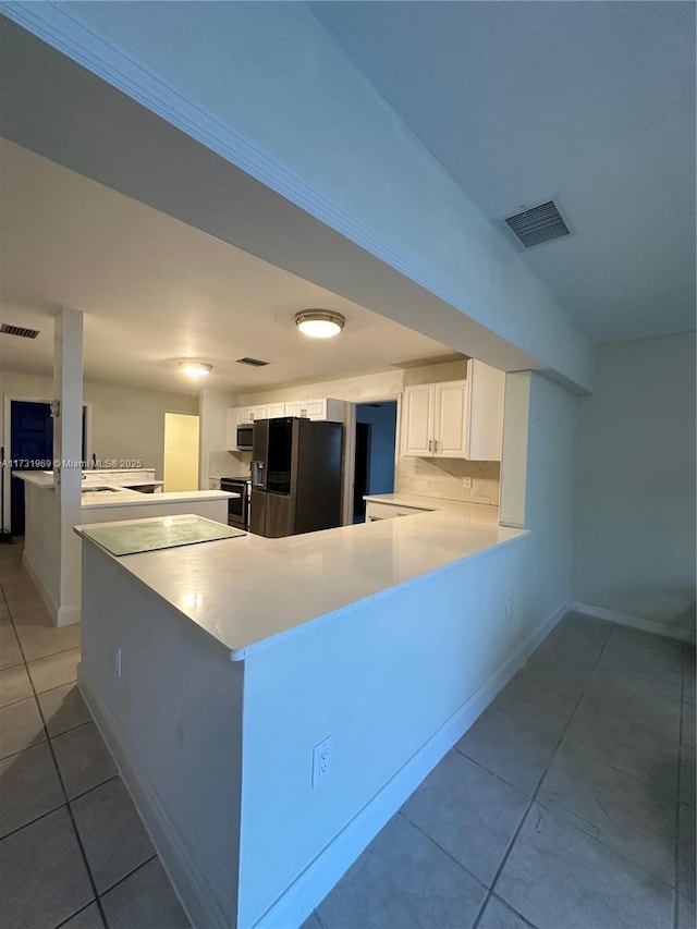 kitchen with light tile patterned flooring, kitchen peninsula, stainless steel appliances, decorative backsplash, and white cabinets