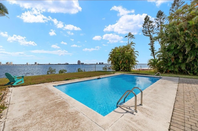 outdoor pool with a patio, a yard, and a water view