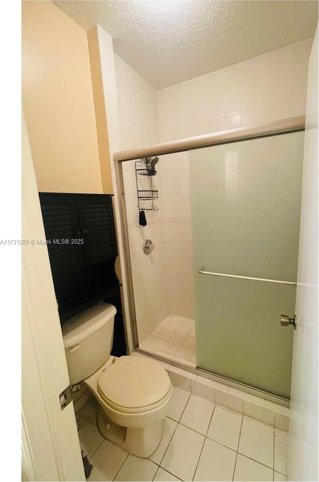 bathroom with a shower with door, tile patterned floors, a textured ceiling, and toilet