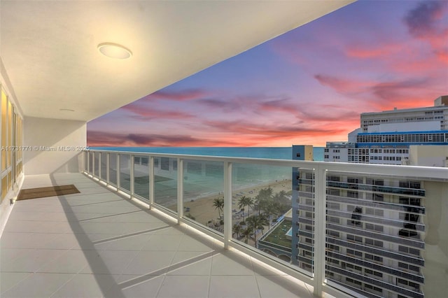 balcony at dusk with a water view and a view of the beach