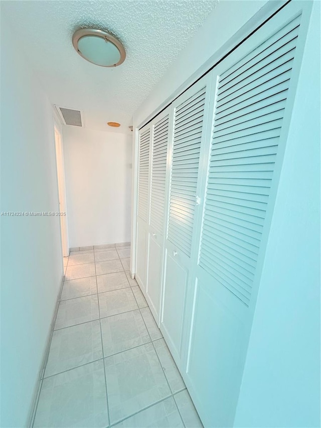 corridor featuring a textured ceiling and light tile patterned floors