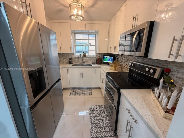 kitchen with white cabinetry, sink, light tile patterned floors, stainless steel appliances, and a textured ceiling