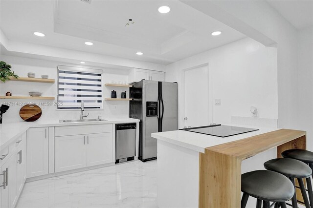 kitchen featuring sink, appliances with stainless steel finishes, white cabinetry, a tray ceiling, and a kitchen bar