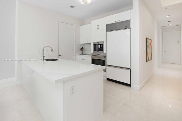 kitchen with sink, kitchen peninsula, paneled fridge, light stone countertops, and white cabinets