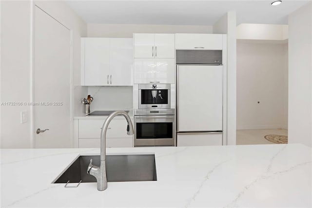 kitchen with sink, white cabinets, paneled built in fridge, light stone countertops, and stainless steel double oven