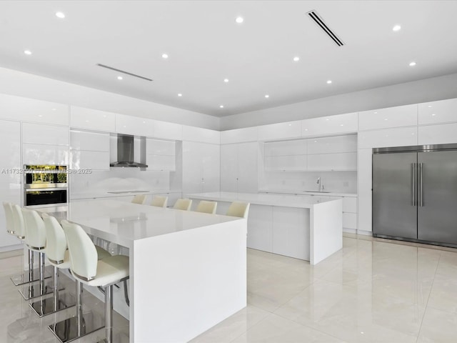 kitchen with wall chimney exhaust hood, a large island, built in fridge, and white cabinets