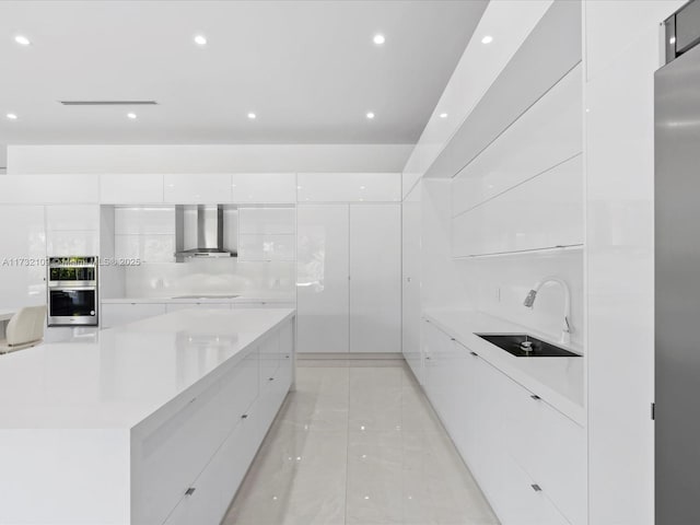 kitchen with cooktop, sink, white cabinetry, stainless steel double oven, and wall chimney range hood