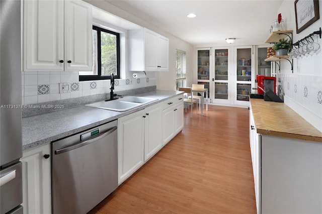 kitchen featuring appliances with stainless steel finishes, white cabinetry, sink, backsplash, and light hardwood / wood-style floors