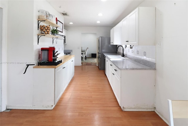 kitchen with light wood-type flooring, sink, tasteful backsplash, and white cabinets