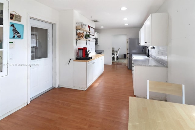 kitchen with wood-type flooring, sink, white cabinets, and stainless steel refrigerator