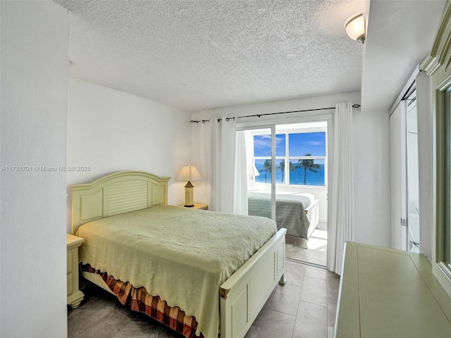 bedroom featuring access to exterior, a water view, a textured ceiling, light tile patterned flooring, and a closet