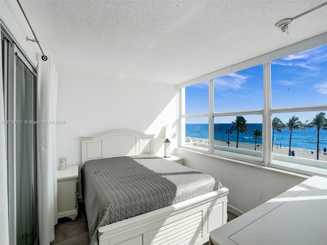 bedroom with multiple windows, a textured ceiling, a view of the beach, and a water view