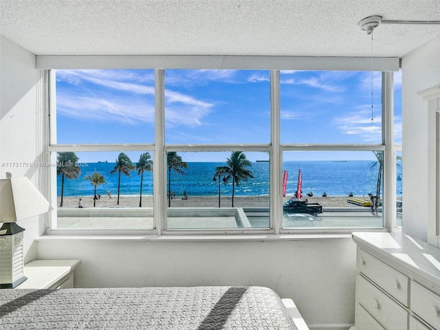 bedroom with a water view, a beach view, and a textured ceiling