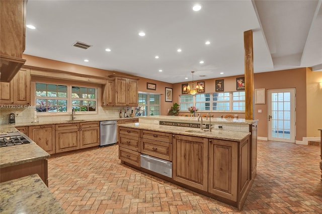 kitchen with pendant lighting, sink, backsplash, stainless steel appliances, and light stone countertops