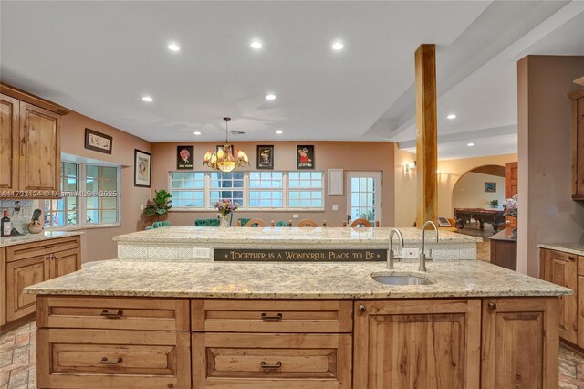 kitchen with a kitchen island with sink, sink, decorative light fixtures, and light stone countertops