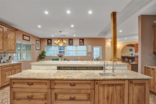 kitchen with pendant lighting, an island with sink, sink, and light stone counters