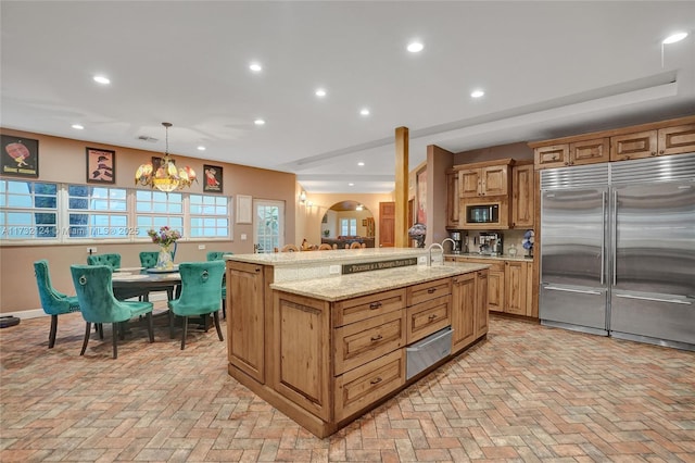 kitchen featuring decorative light fixtures, a chandelier, built in appliances, light stone counters, and a spacious island