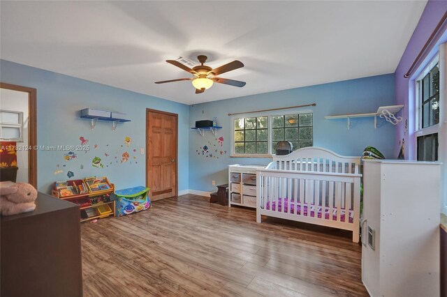 bedroom featuring a crib, wood-type flooring, and ceiling fan