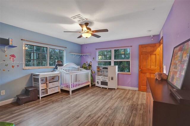 bedroom with hardwood / wood-style flooring, a crib, and ceiling fan