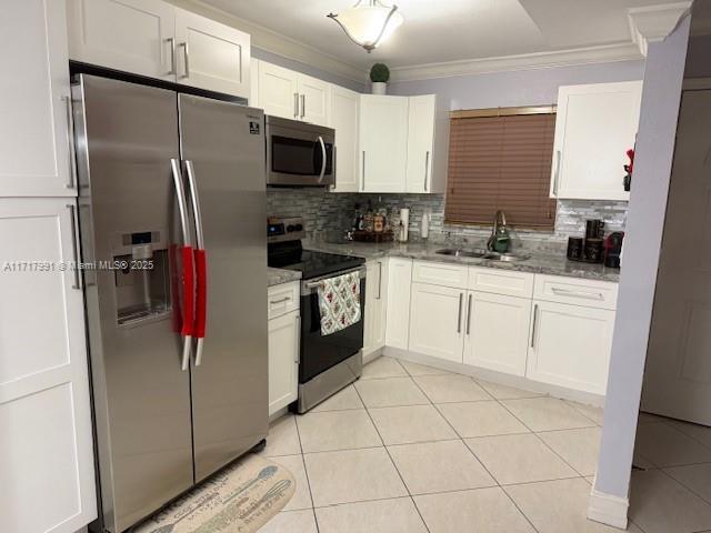 kitchen featuring sink, light tile patterned floors, appliances with stainless steel finishes, ornamental molding, and white cabinets