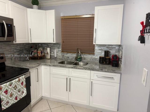 kitchen featuring appliances with stainless steel finishes, sink, white cabinets, light tile patterned floors, and light stone counters