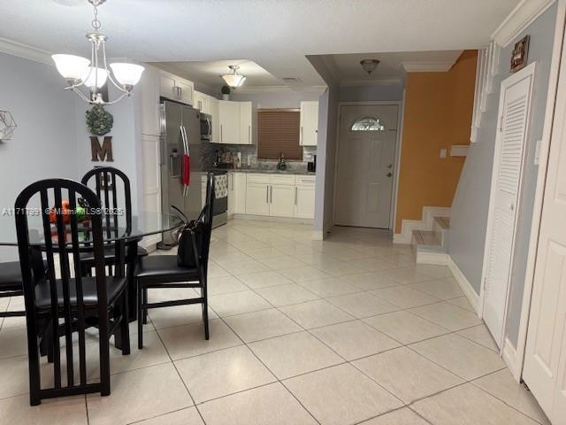 dining area with crown molding, sink, an inviting chandelier, and light tile patterned floors