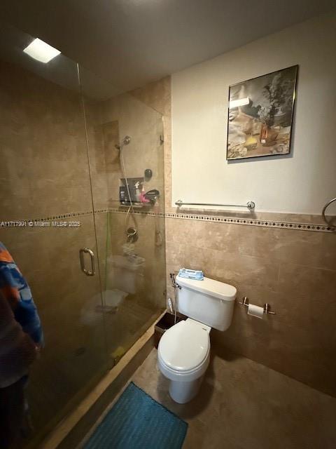 bathroom featuring toilet, a shower with shower door, and tile walls