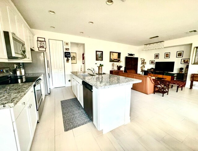 kitchen with sink, light stone counters, stainless steel appliances, a kitchen island with sink, and white cabinets