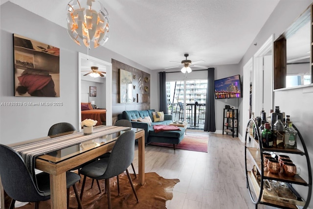 dining area featuring hardwood / wood-style flooring, ceiling fan with notable chandelier, and a textured ceiling