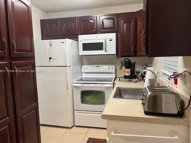 kitchen featuring sink, light tile patterned floors, a textured ceiling, and white appliances