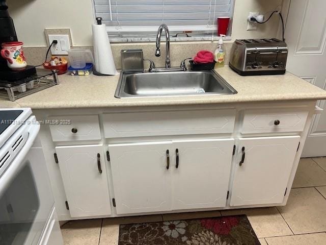 kitchen featuring white electric range, sink, light tile patterned floors, and white cabinets