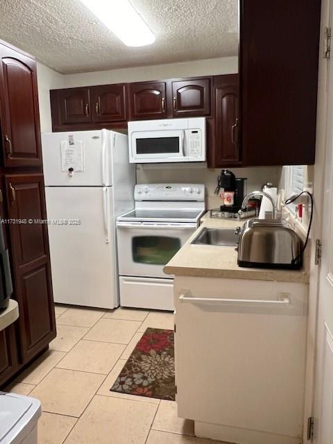 kitchen with sink, light tile patterned floors, white appliances, dark brown cabinetry, and a textured ceiling