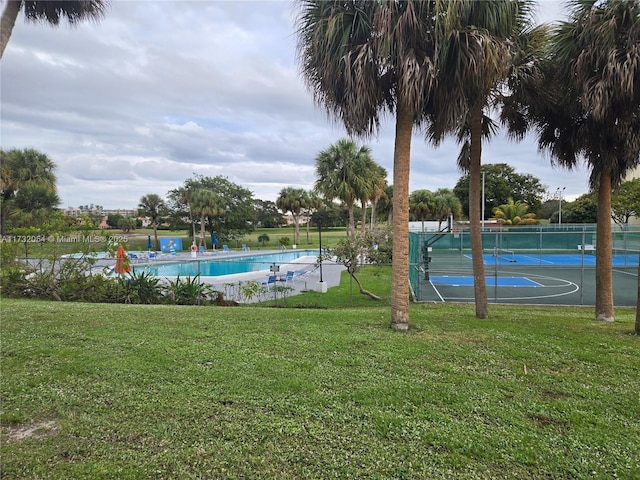 view of swimming pool featuring a yard and basketball hoop