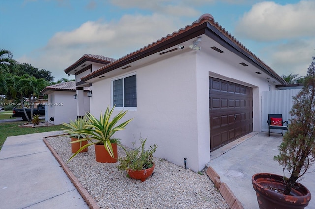 view of side of property with a tile roof, an attached garage, and stucco siding