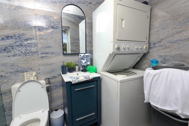 clothes washing area with stacked washing maching and dryer and tile walls