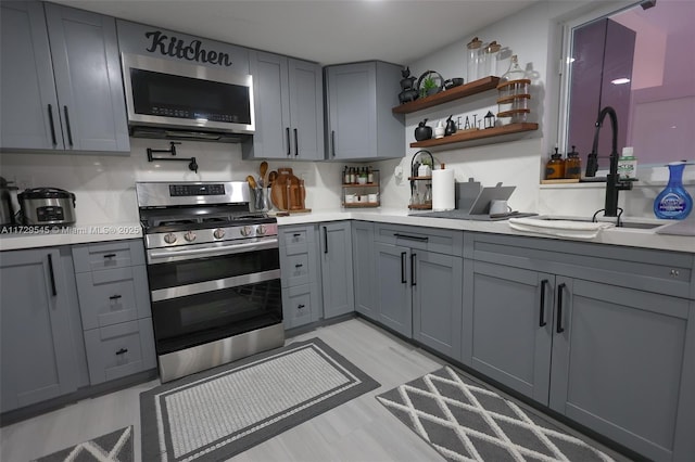 kitchen featuring gray cabinets, stainless steel appliances, a sink, and light countertops